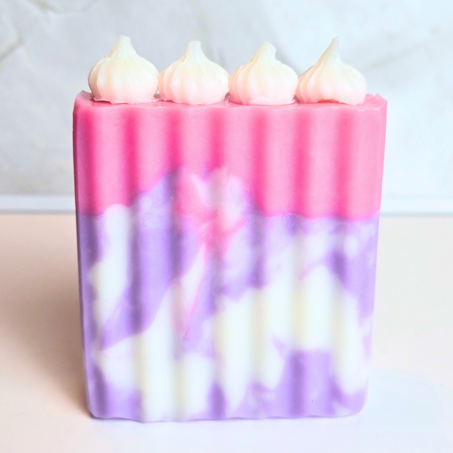 Artisan soap resembling a birthday cake in pink and purple hues, front view.