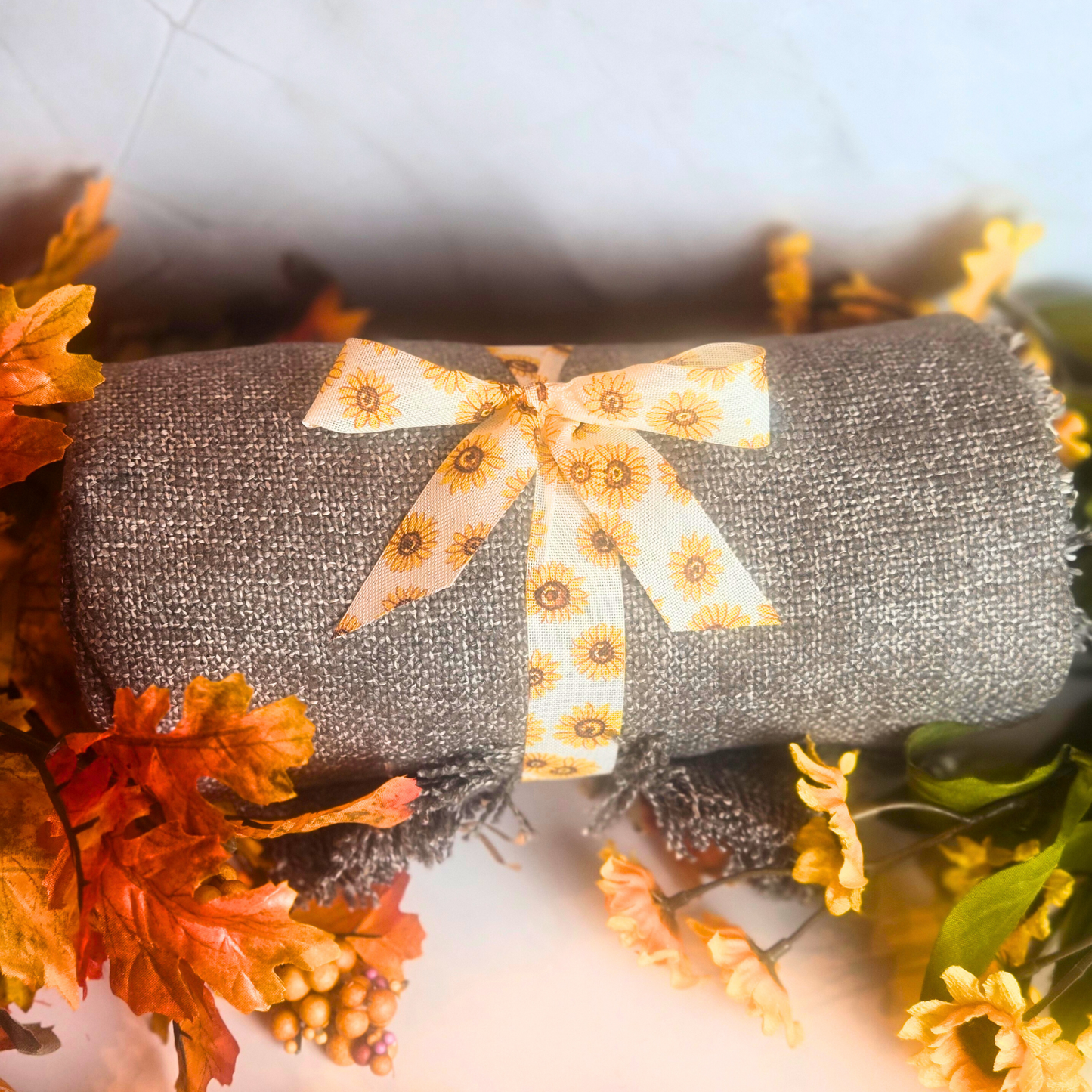 Gray throw with a decorative bow surrounded by autumn leaves and flowers.