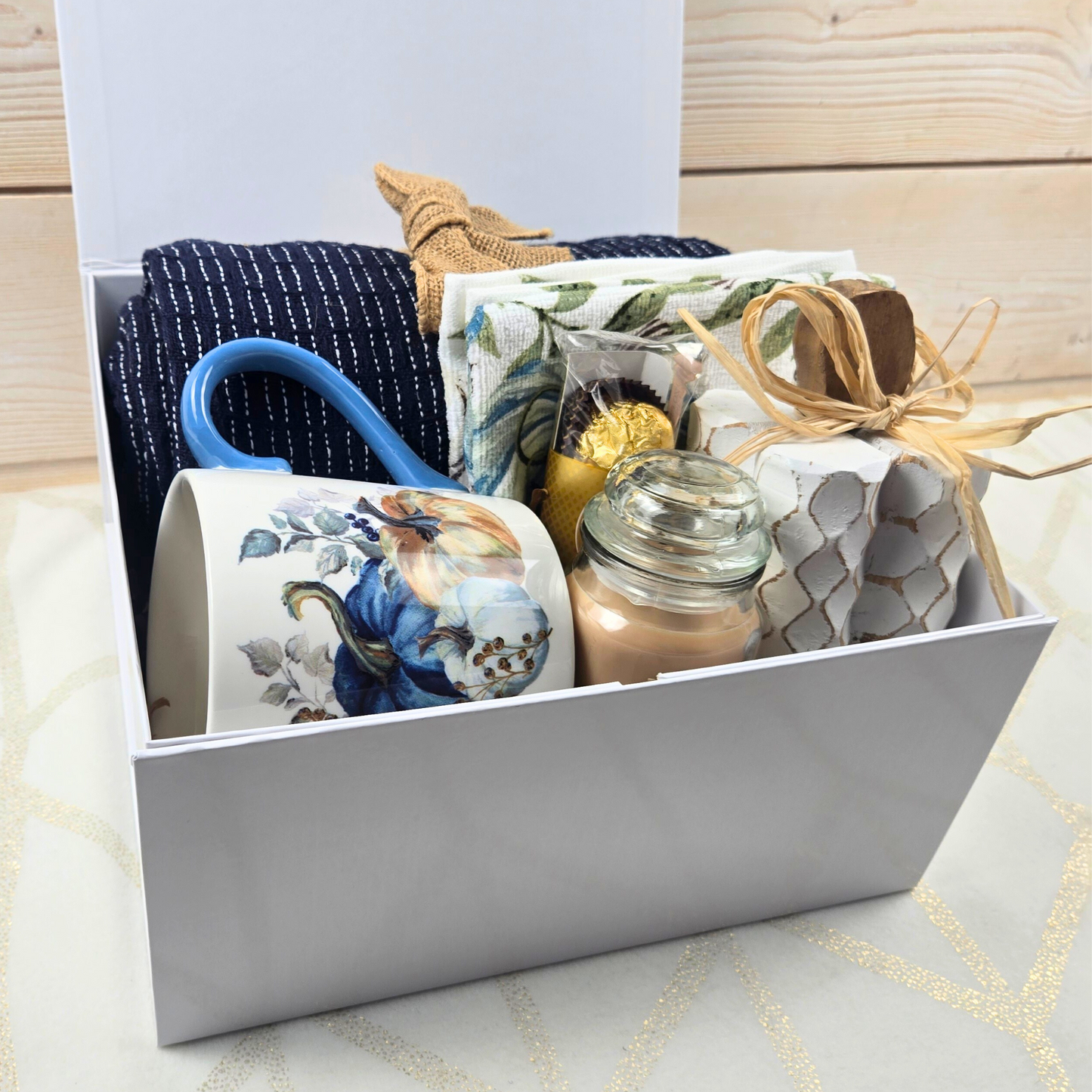 Cozy Fall Gift Box for Her with Elegant Blue Accents and Magnet Closure with navy blue throw, 16 oz mug, blue pumpkin dish towel, 3 oz pumpkin maple custard candle, white pumpkin decor and Ferrero Rocher.