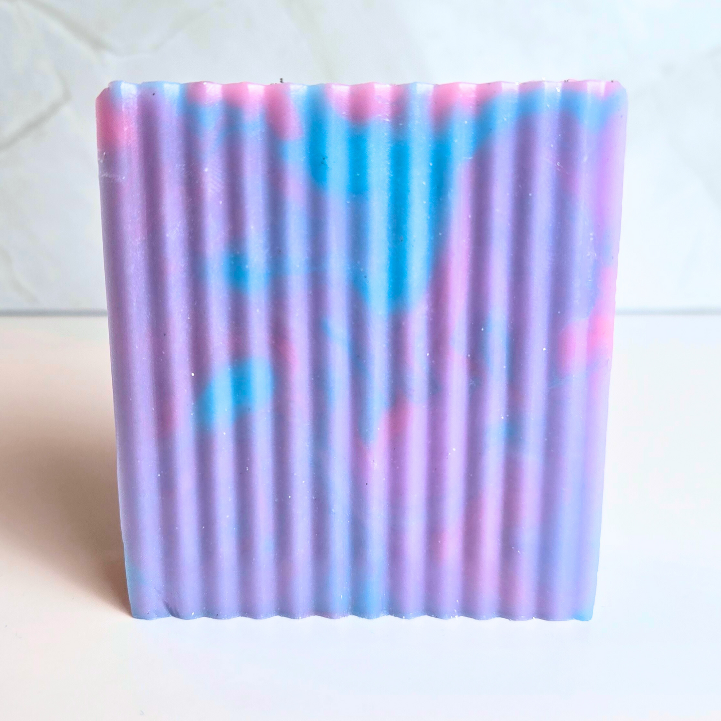 Shimmery blue, purple, and pink handmade soap for luxurious skincare, front view.
