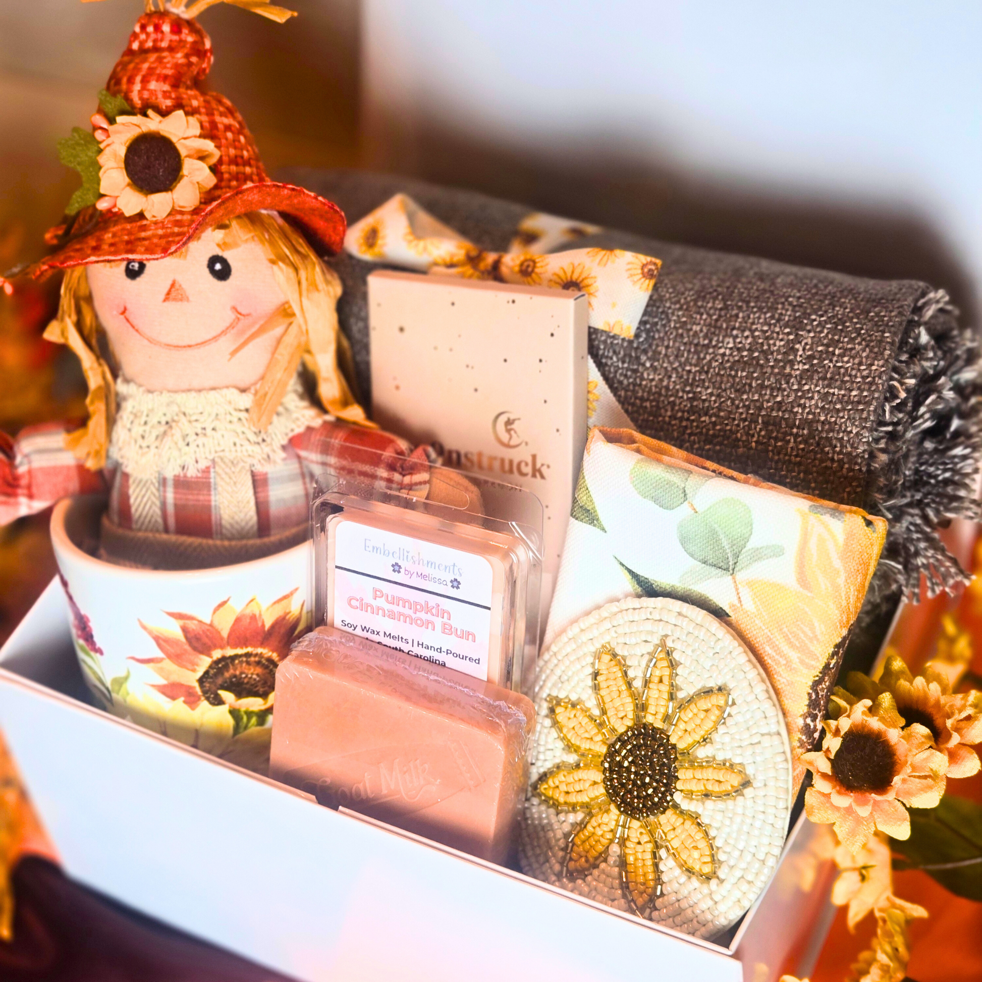 Gift box with decorative items including a scarecrow, wax melts, and sunflower-themed decor.