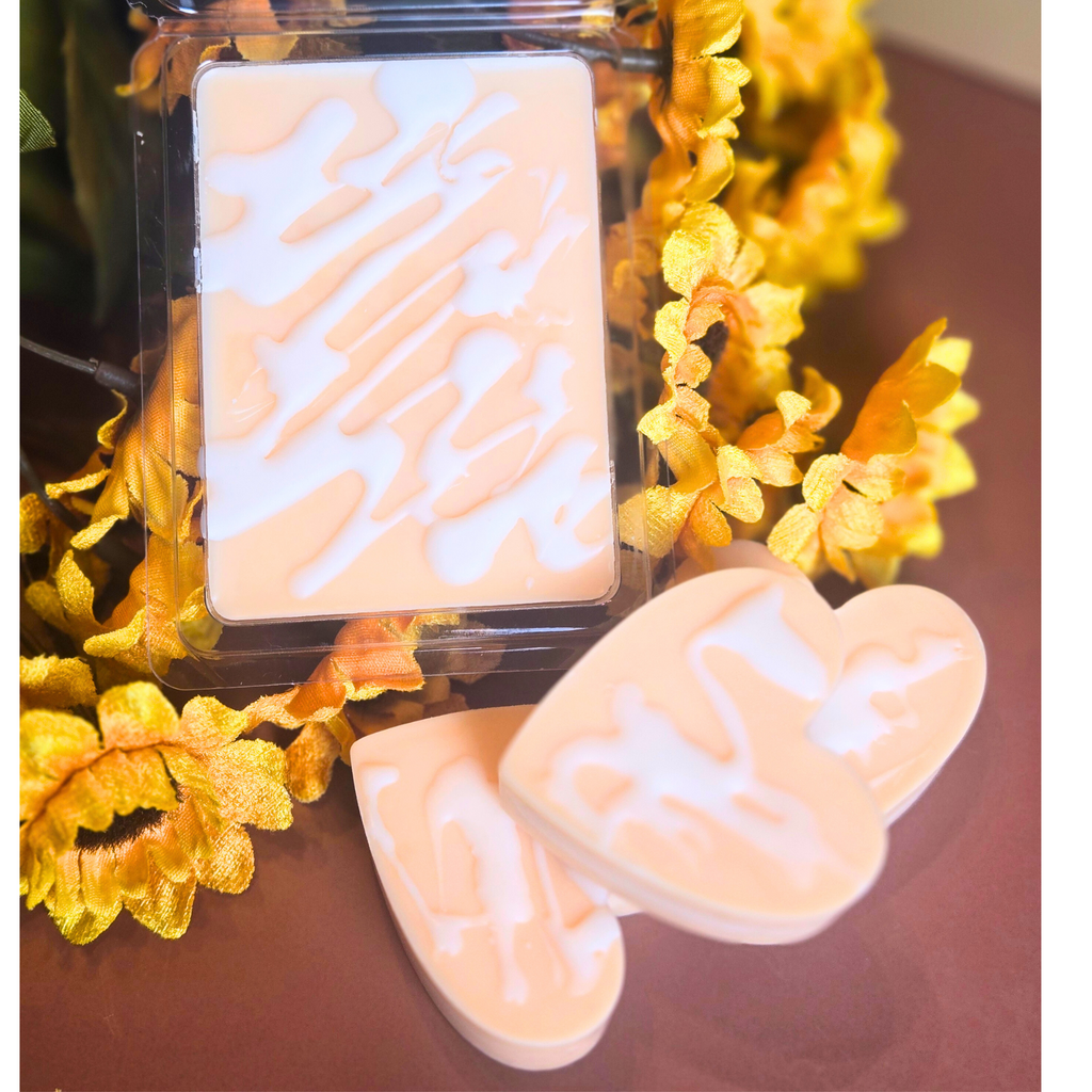 Soy wax melt clamshell labeled “Pumpkin Cinnamon Bun” with fall flowers in background, top view.