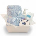 Baby gift set in a white box lined with white tissue paper, featuring a light blue plush blanket tied with a matching ribbon, a baby bottle, and a bib with blue elephant prints.