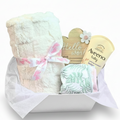 A baby gift basket set in a white box with tissue paper, featuring a fluffy cream blanket tied with a pink ribbon, 2 bibs, a wooden heart sign that reads 'Hello world', and an Aveeno baby lotion.