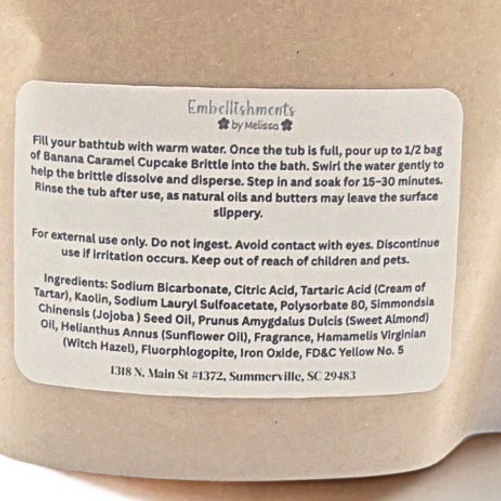 A close-up of a beige paper bag with a white product label reading 'Embellishments by Melissa' and product instructions for banana caramel cupcake brittle.