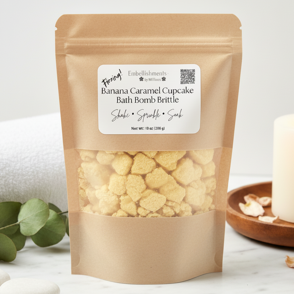 A kraft paper stand-up pouch of Banana Caramel Cupcake Bath Bomb Brittle by Fungal Embellishments, shown on a light marble surface with a white candle, green leaves, and a wooden dish in the background.