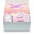 A curated birthday gift box set from The Embellishment Table, featuring a plush pink ribbed blanket tied with a purple ribbon,a pink soap bar, wax melts and cozy socks.