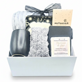 A curated gift box set containing a black cup, gray textured socks, a black and gold purse tied with a sheer black ribbon, a beige chocolate bar labeled moonstruck, and a white soap bar, arranged in a white magnetic box.