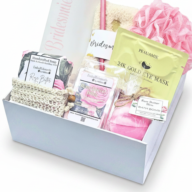 A curated bridal gift box containing a white box filled with bath and beauty items including a pink bath bomb, rose butter soap, 24K Gold Eye Mask, and a pink bath pouf.