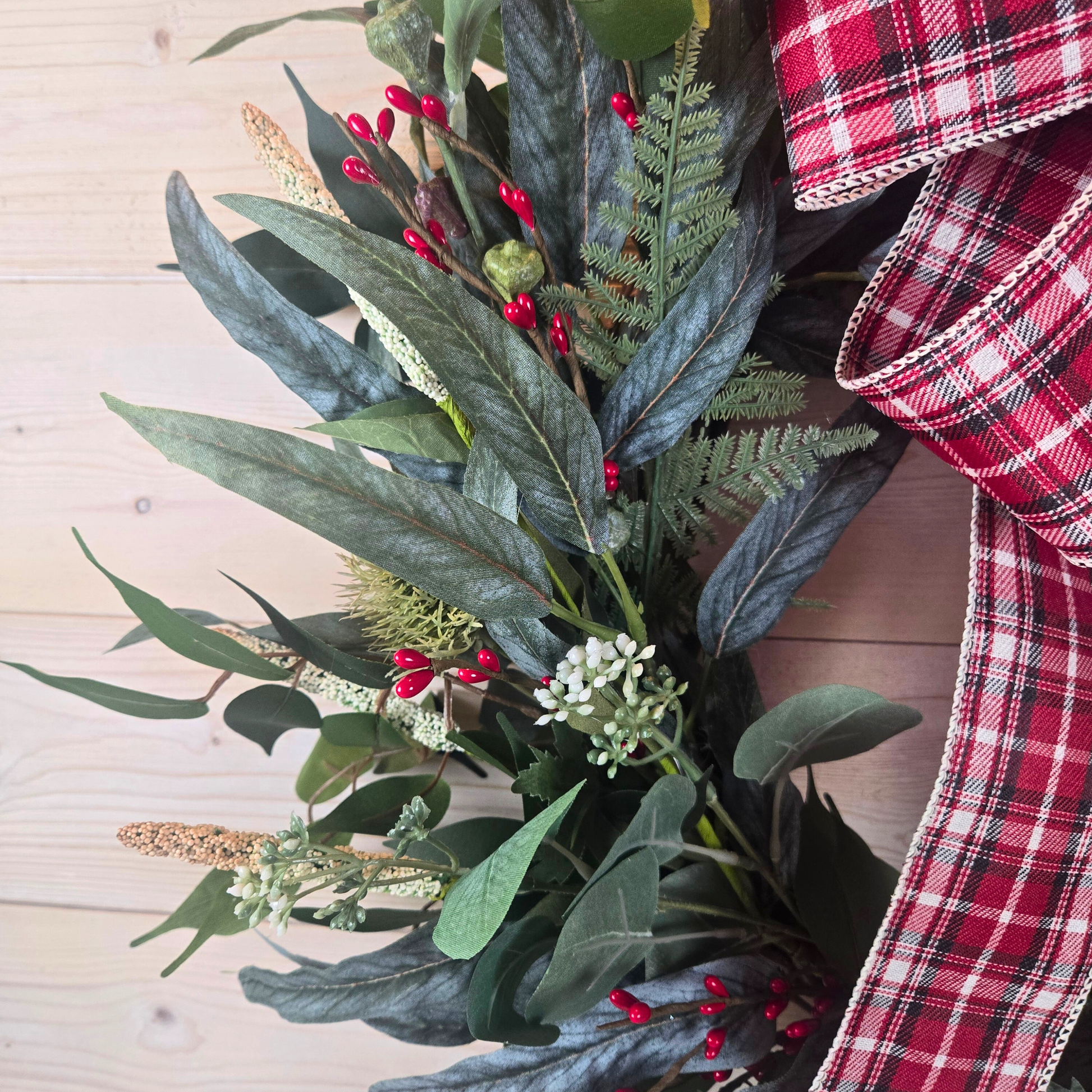 Christmas wreath with red berries and buffalo plaid bow.