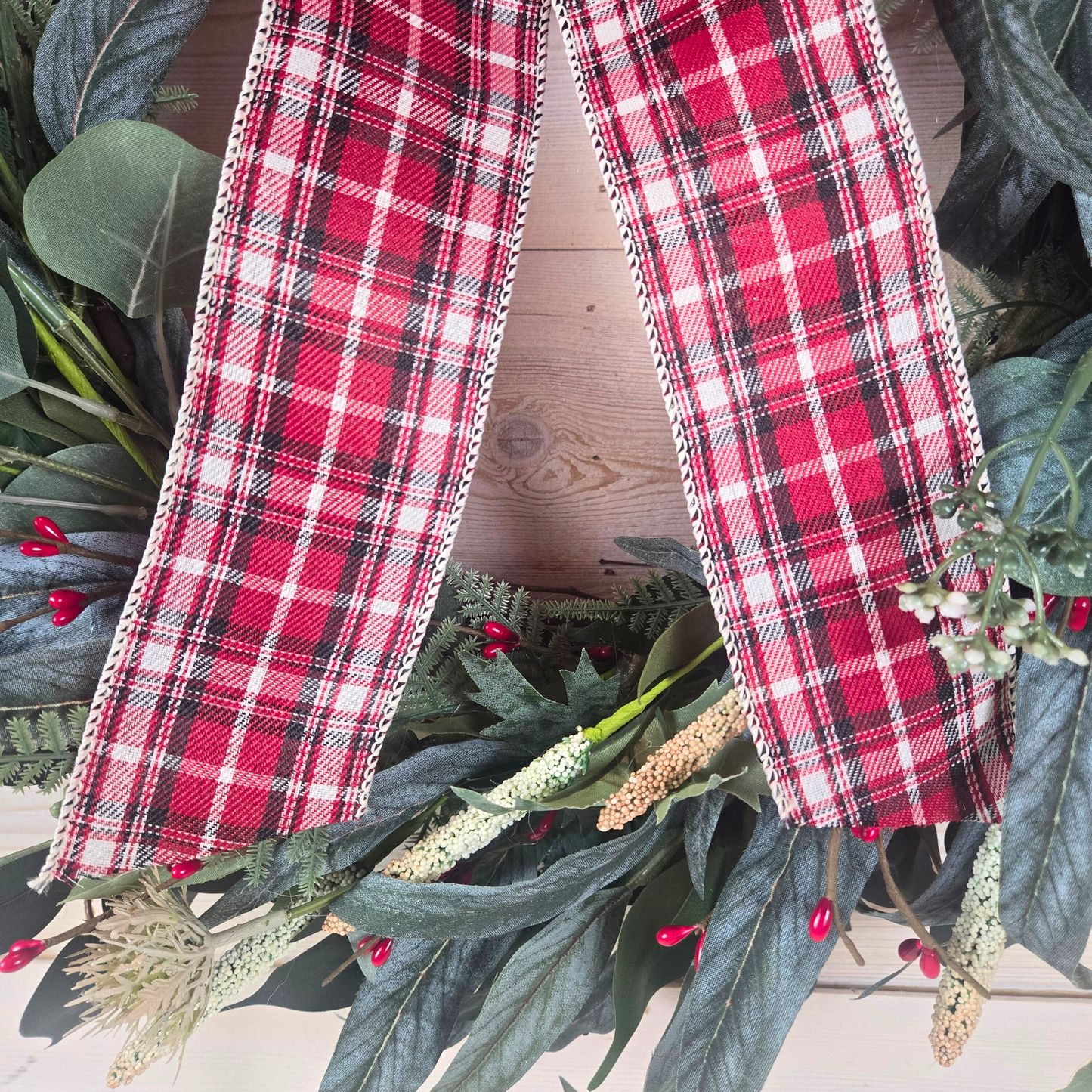 Christmas wreath with red berries and buffalo plaid bow.