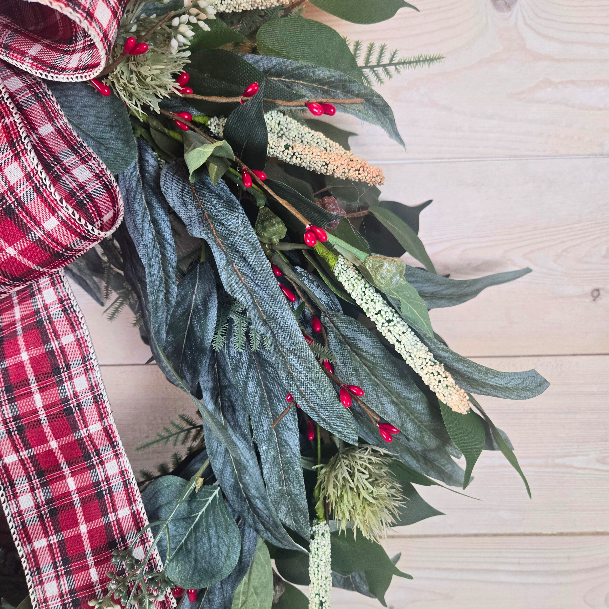 Christmas wreath with red berries and buffalo plaid bow.