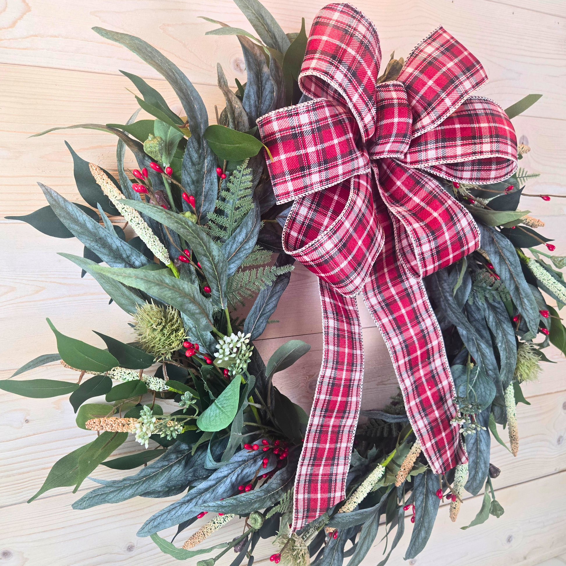 Christmas wreath with red berries and buffalo plaid bow.