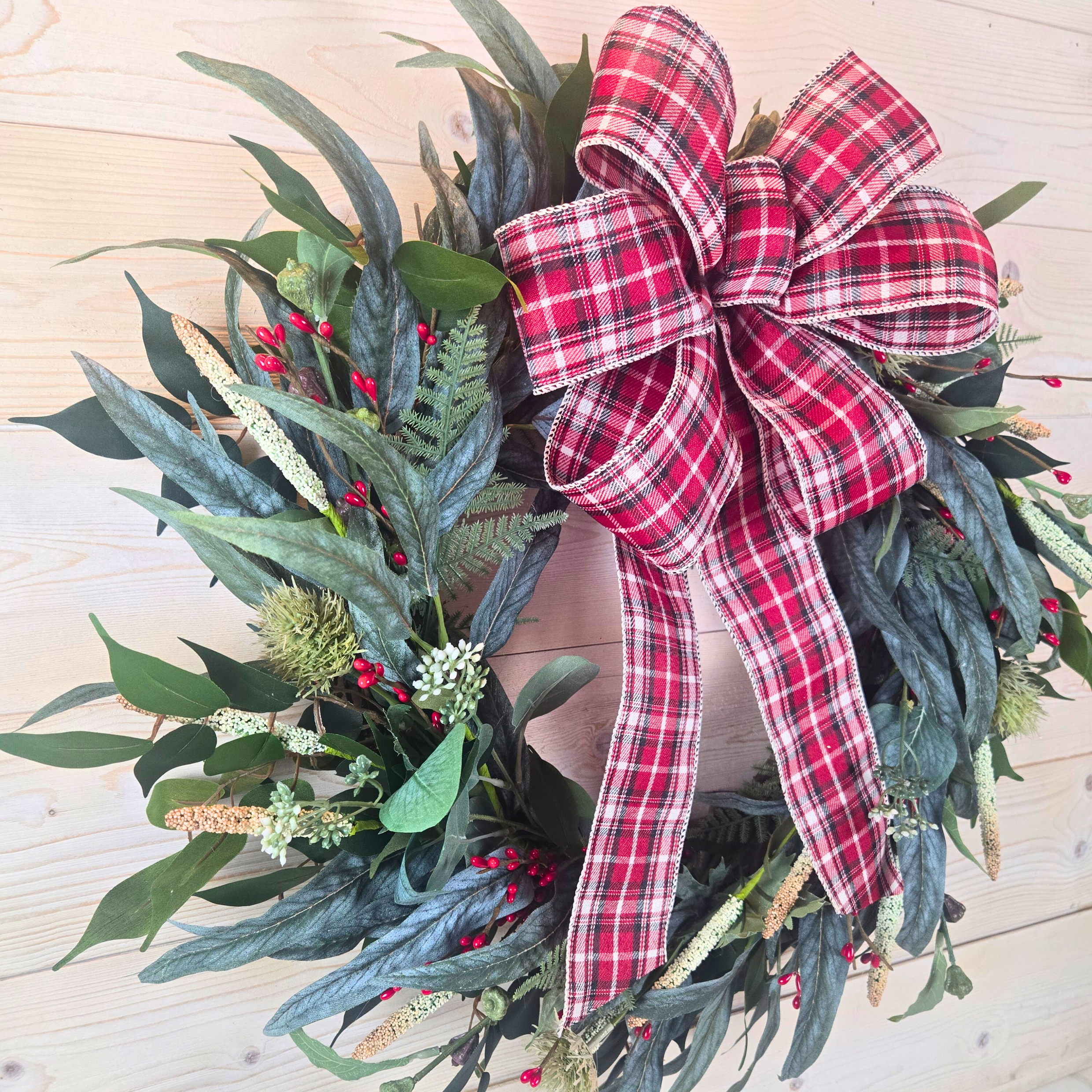 Christmas wreath with red berries and buffalo plaid bow.