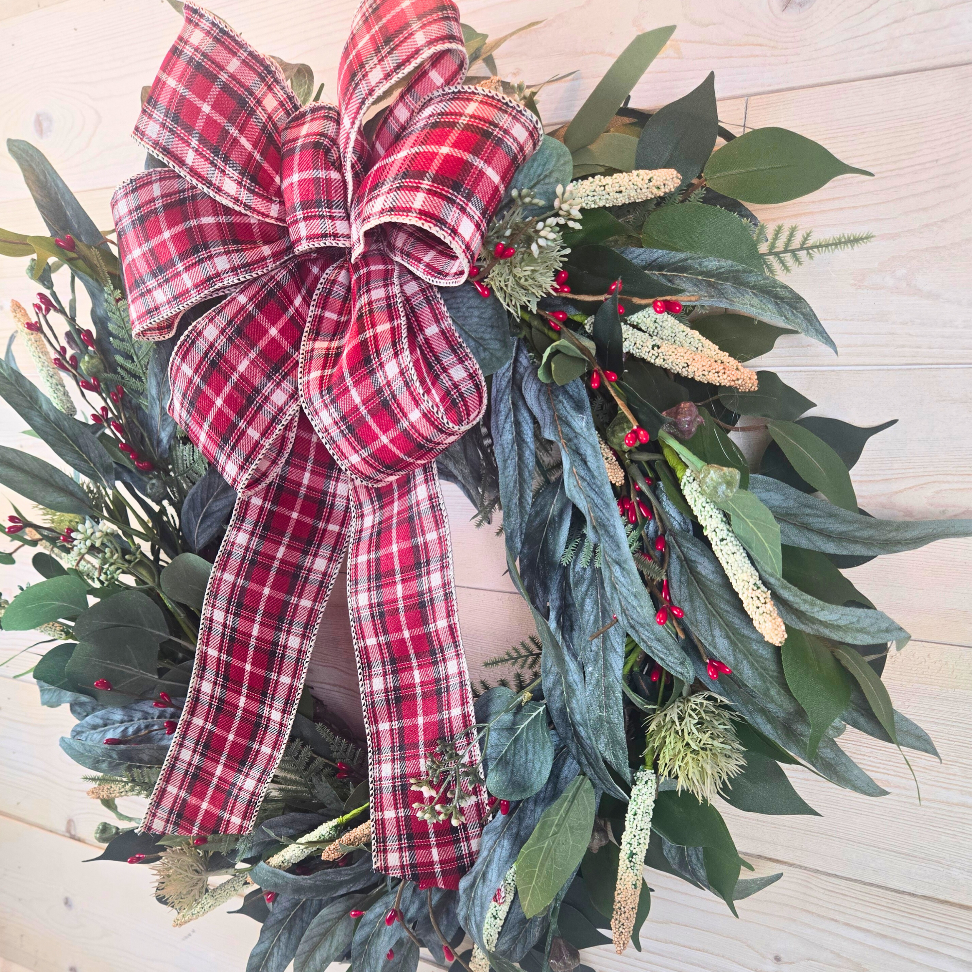 Christmas wreath with red berries and buffalo plaid bow.