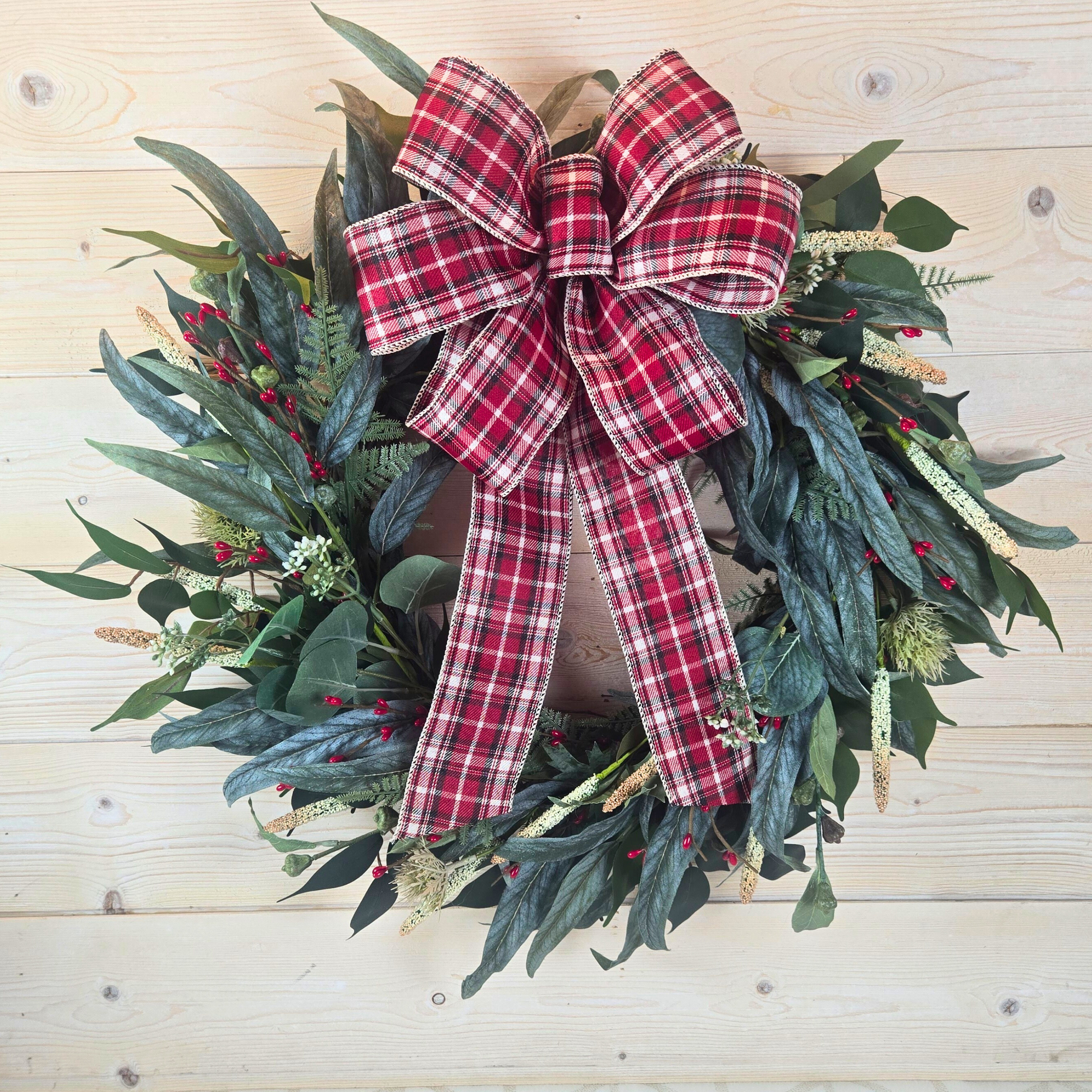 Christmas wreath with red berries and buffalo plaid bow.