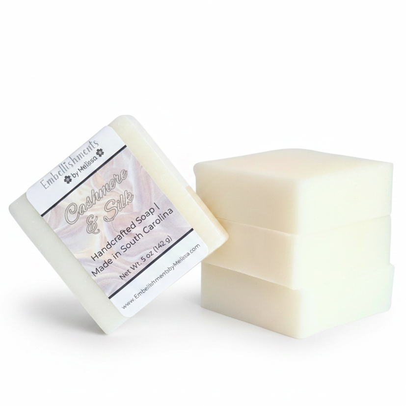 Three rectangular bars of off-white soap standing upright, with one bar leaning against them and showing a white label 'Handcrafted Soap Made in South Carolina.'