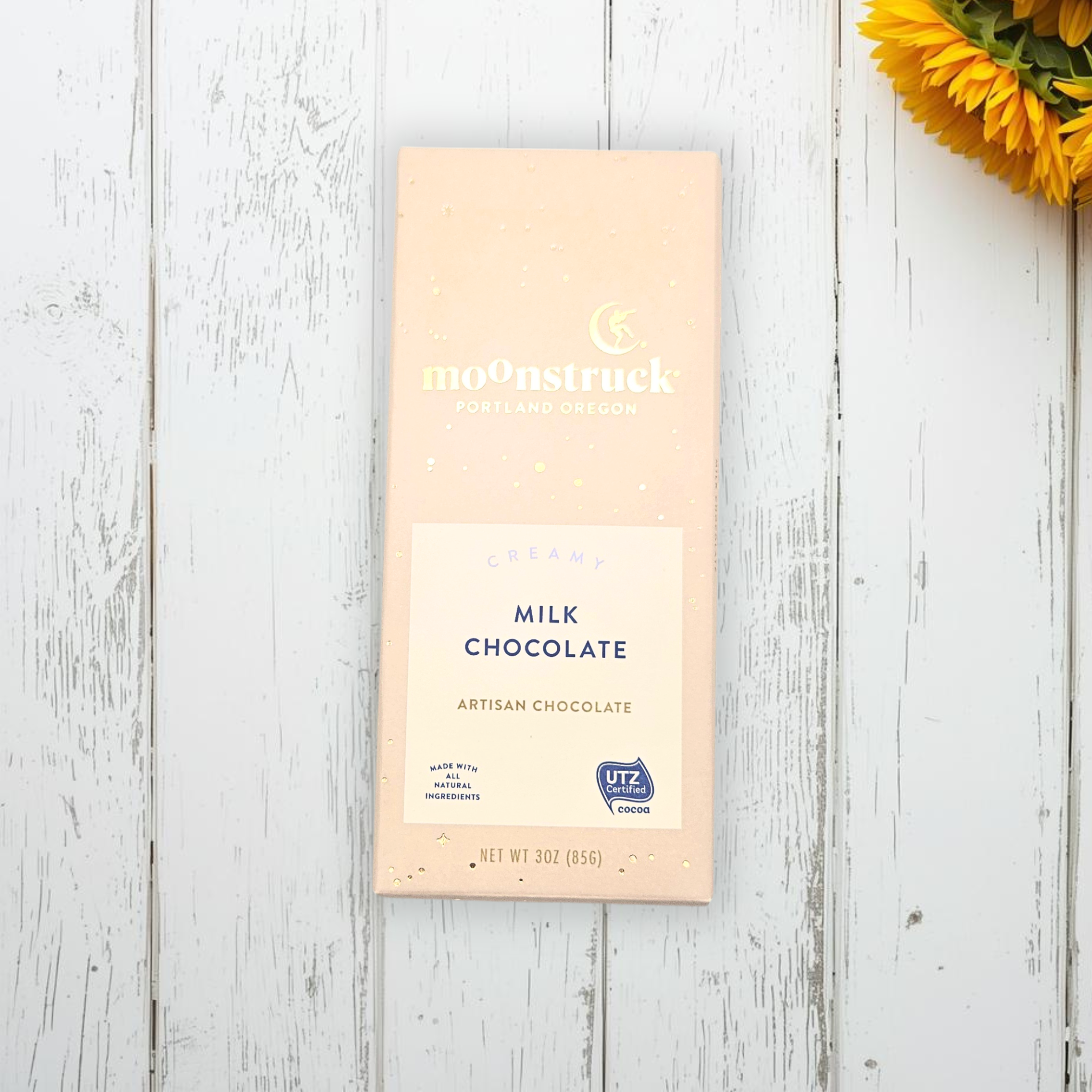 Moonstruck milk chocolate bar on a wooden surface with a sunflower.