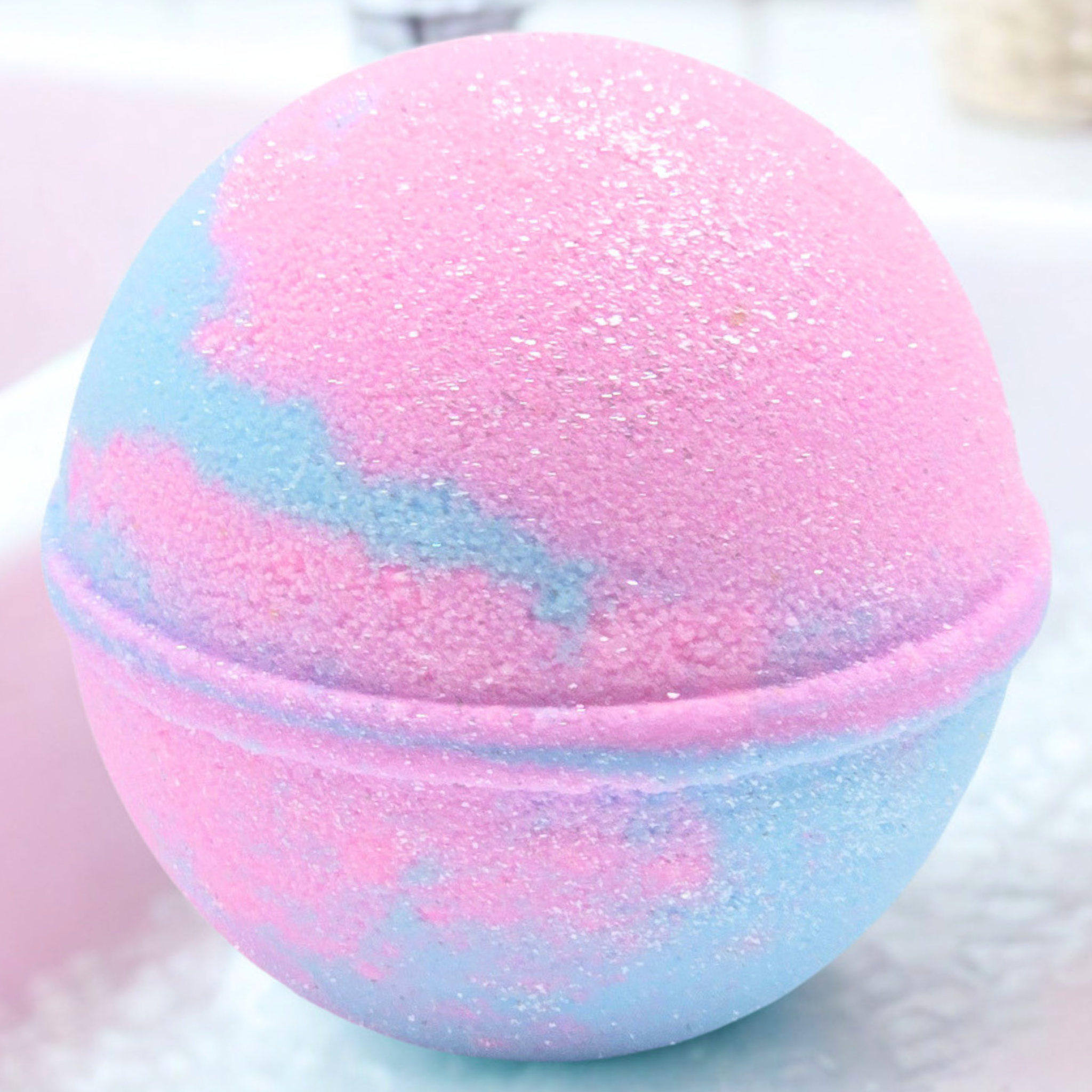 A spherical bath bomb with a pink and light blue marbled pattern, covered in fine glitter, shown in a close-up shot.