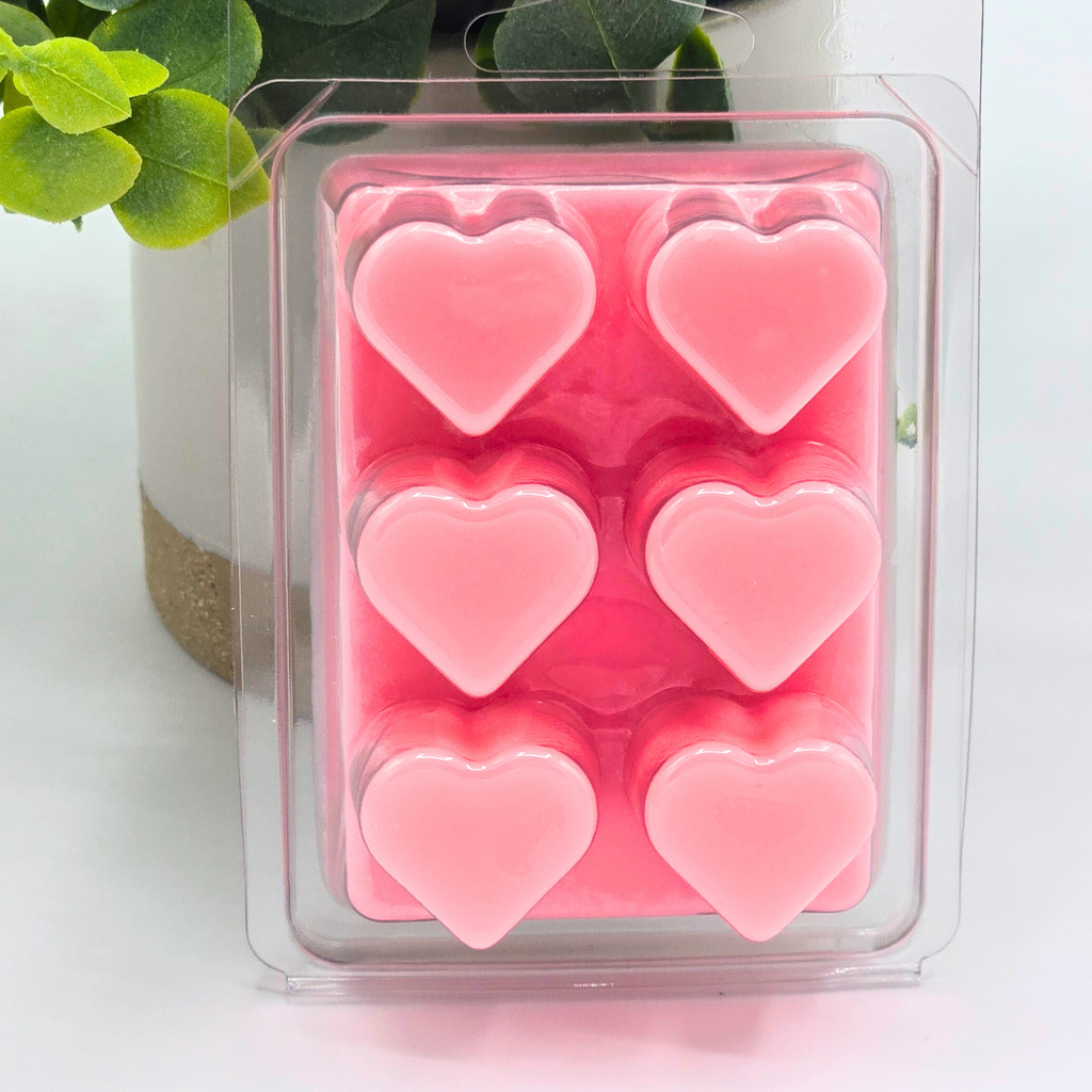 Pink heart-shaped wax melts in a clear mold with greenery in the background