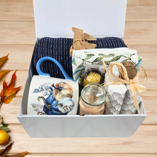 Cozy Fall Gift Box for Her with Elegant Blue Accents and Magnet Closure with navy blue throw, 16 oz mug, blue pumpkin dish towel, 3 oz pumpkin maple custard candle, white pumpkin decor and Ferrero Rocher.