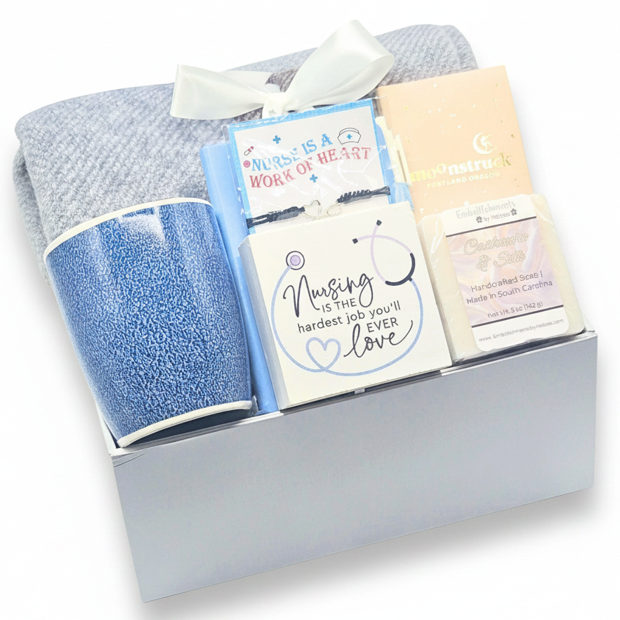 A nursing-themed gift set in a white magnetic box, featuring a blue textured mug, a gray and blue blanket with a white ribbon bow, a bracelet with card that reads 'Nurse is a Work of Heart',  decor that says 'Nursing is the hardest job you'll ever love', handcrafted soap, and a chocolate bar.