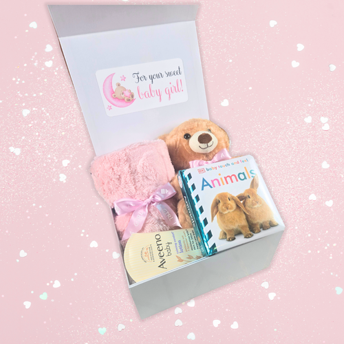 Pink-themed baby girl gift box with plush teddy bear, cozy blanket, lotion and bedtime book, side view.