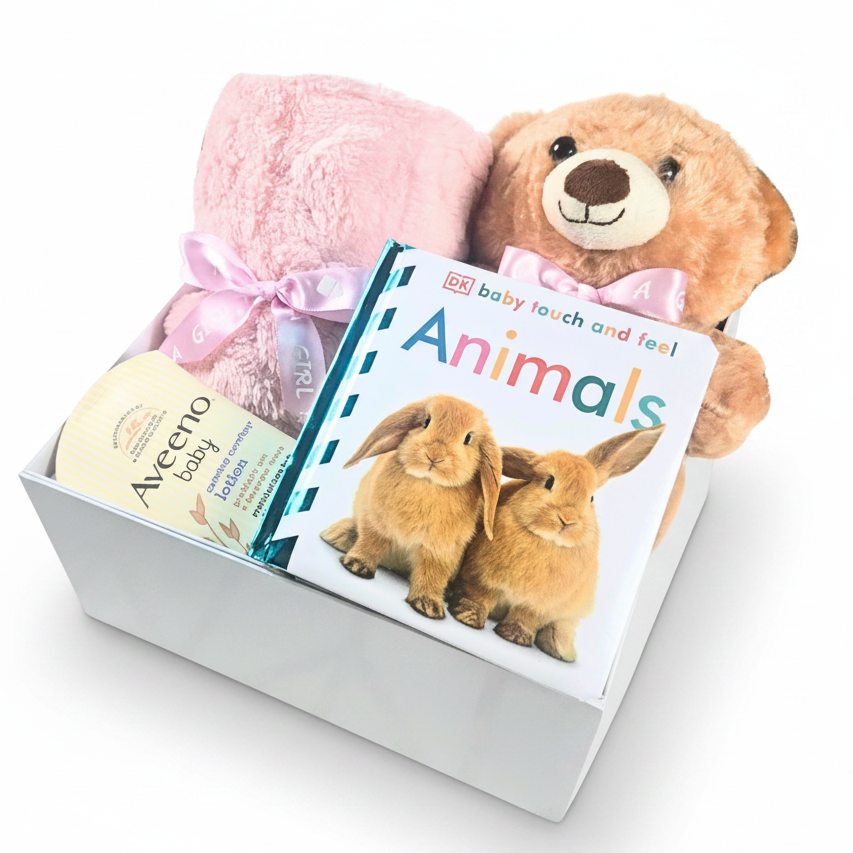 A baby gift set in a white box featuring a pink plush blanket with a pink ribbon, a brown teddy bear, a touch and feel book, and a tube of Aveeno baby lotion.
