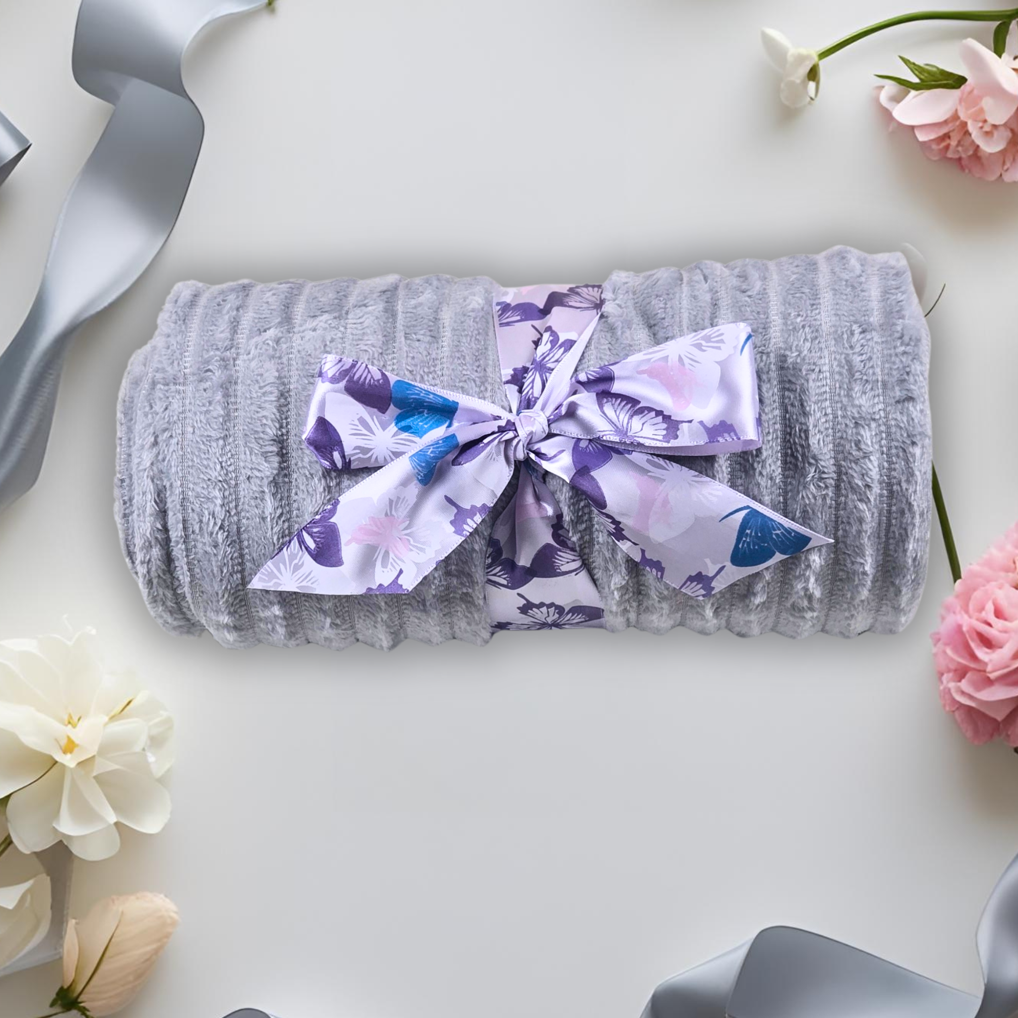 Gray throw rolled up with a butterfly ribbon on a light surface with flowers and ribbons around