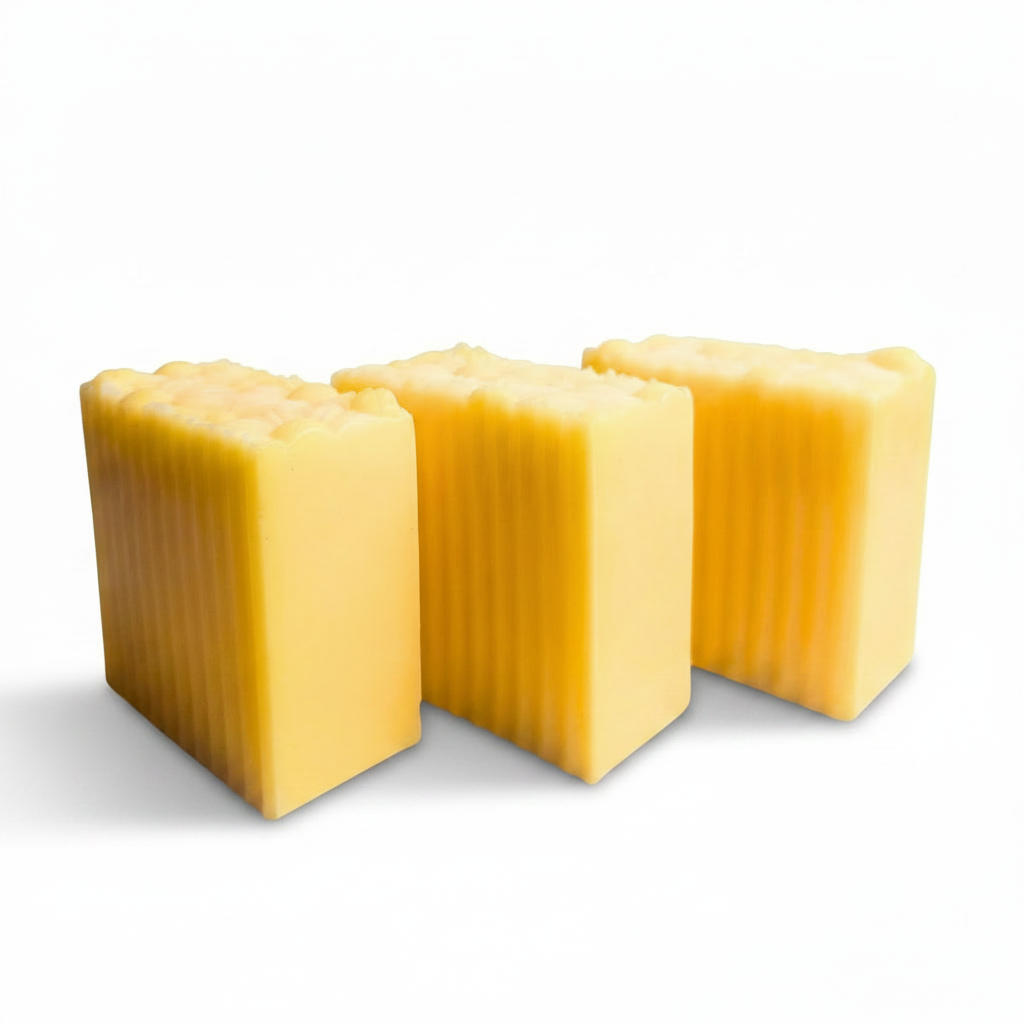Three rectangular bars of yellow soap with vertical grooves, arranged on a white marble tray against a white background.