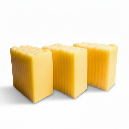 Three rectangular bars of yellow soap with vertical grooves, arranged on a white marble tray against a white background.