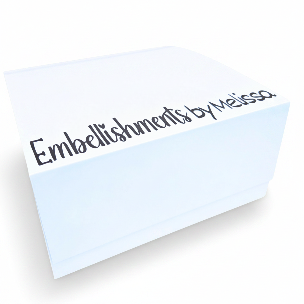 A white rectangular box with the text 'Embellishments by Melissa' printed in dark brown script along the bottom edge, shown on a white background.