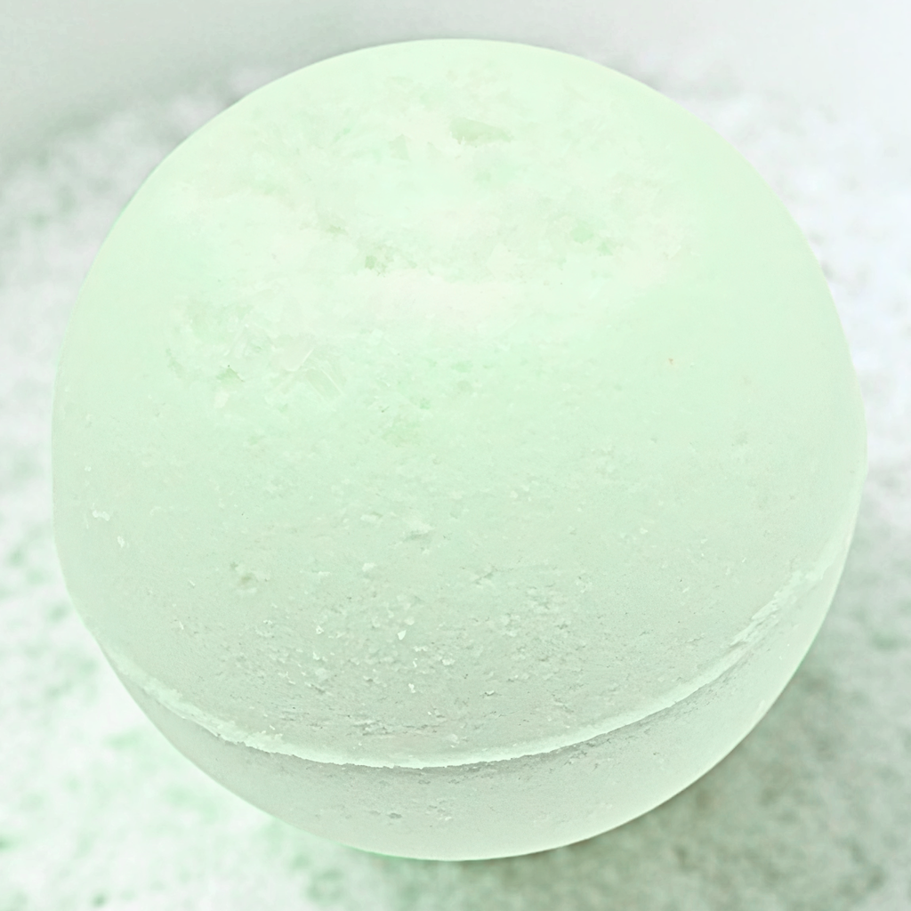 A pale mint green bath bomb sphere with a textured, porous surface, resting on a bed of white bath salts.