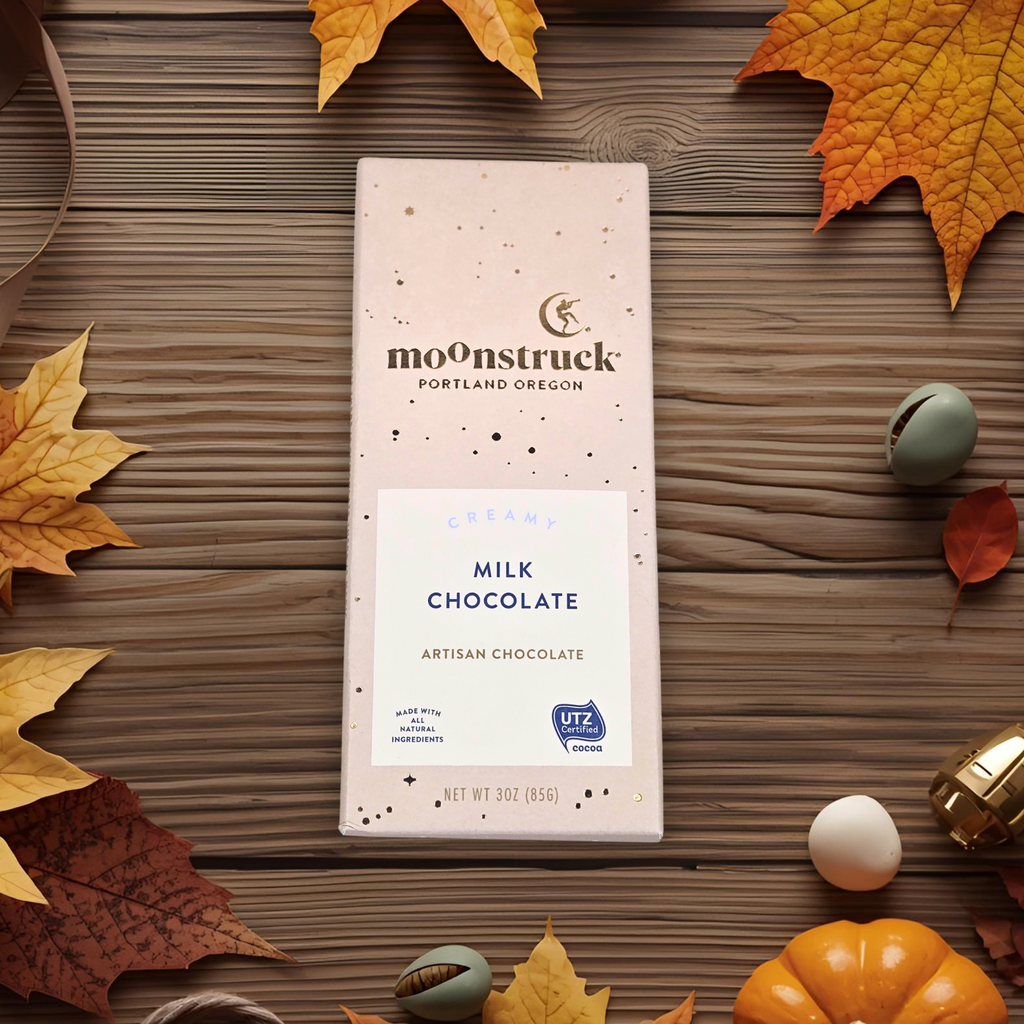 Milk chocolate bar on a wooden surface with autumn leaves and pumpkins.