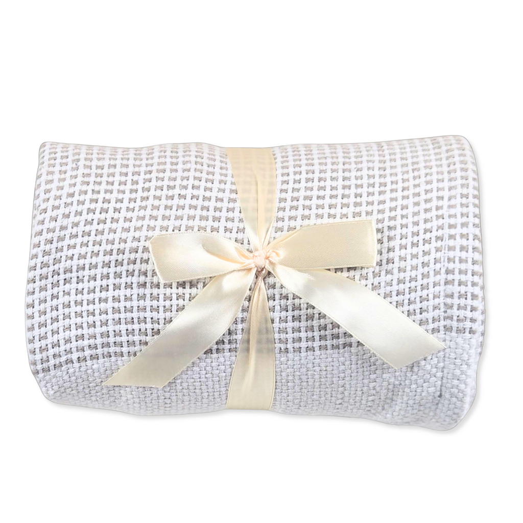 A blanket with a lbeige and white pattern, wrapped in a cream satin ribbon with a bow, on a white background.