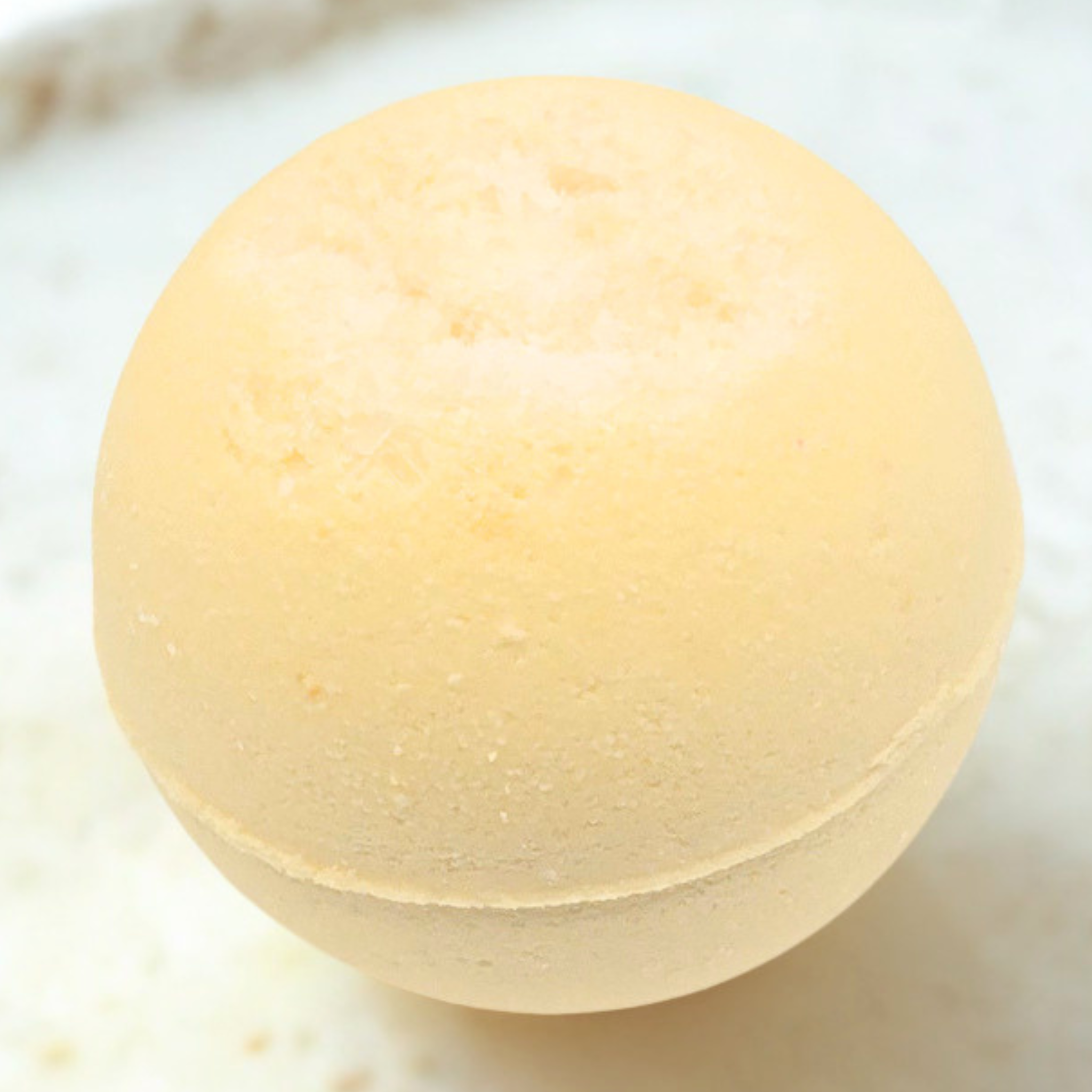 A round, pale yellow bath bomb with a textured, porous surface, resting on a light, neutral background.