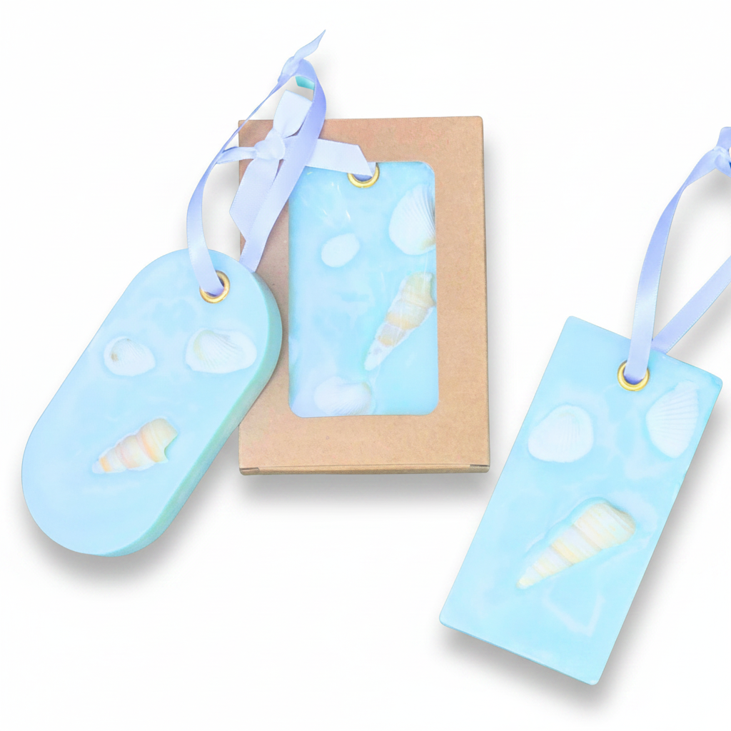 Three light blue soap tags with seashell designs and white ribbons on a white background.