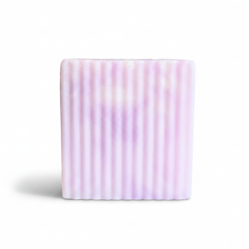 A rectangular bar of soap with vertical ridges, featuring a soft lavender coloration, set against a plain white background.