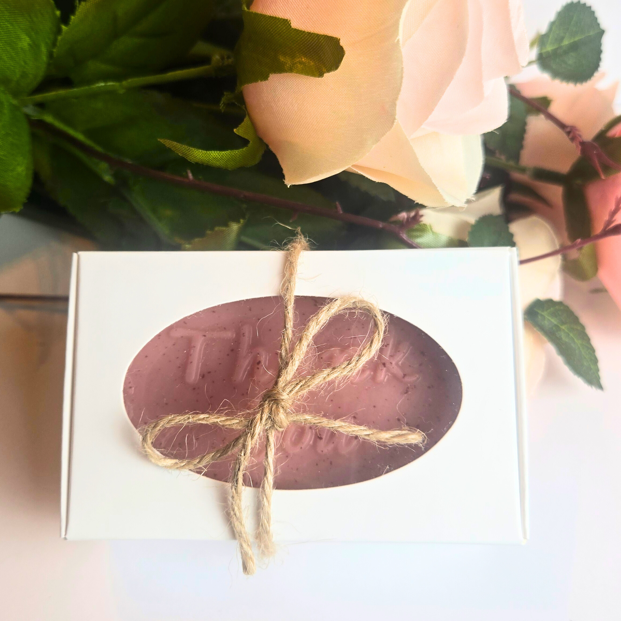 Rose-colored soap bar with smooth texture, wrapped as a guest favor and scented with Love Spell, top view.