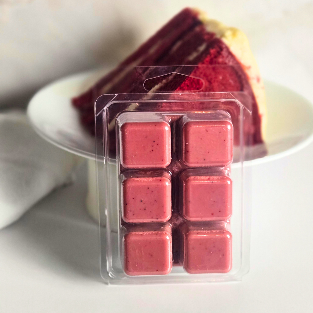 Red velvet soy wax cubes next to red velvet cake on a white surface.
