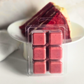 Red velvet soy wax cubes next to red velvet cake on a white surface.