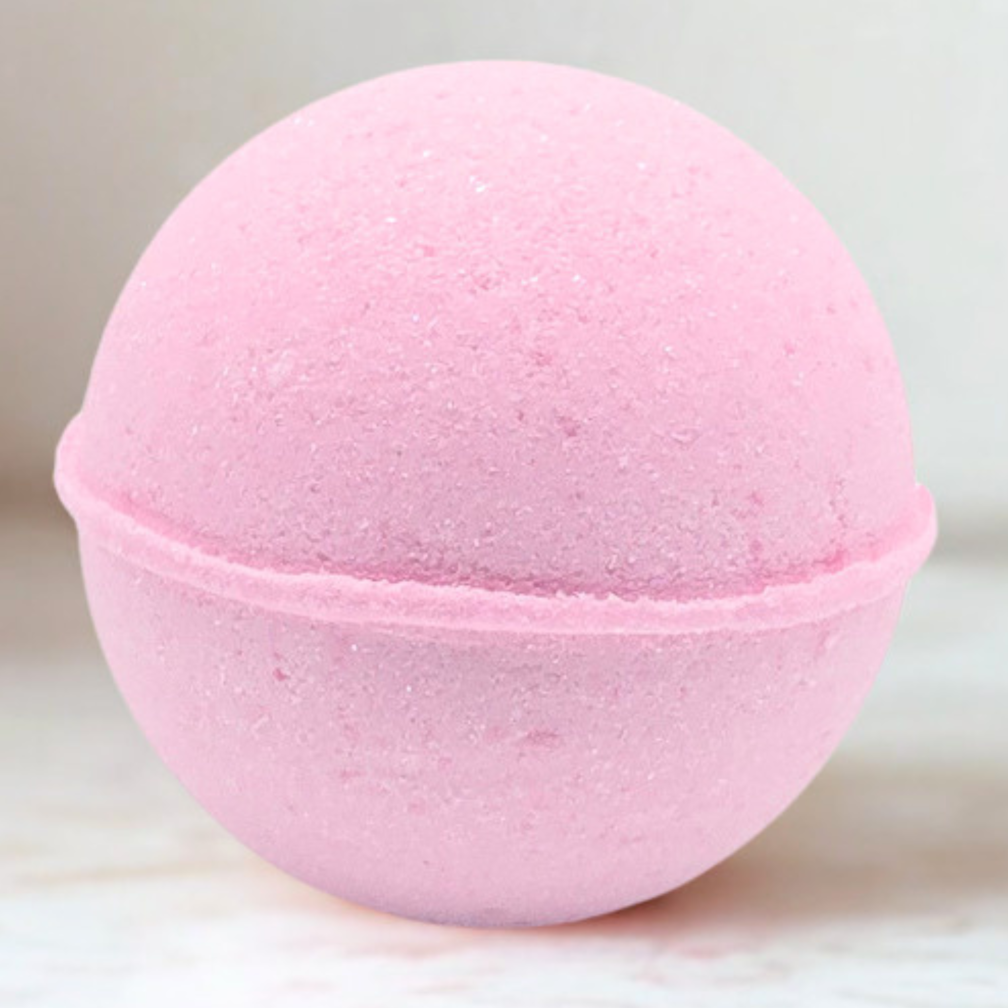 A pink spherical bath bomb with a textured, porous surface, shown in a close-up shot against a light, neutral background.