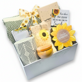 A curated gift box filled with sunflower-themed and neutral-toned items, including a patterned mug, a candle, a floral ribbon, and a greeting card.