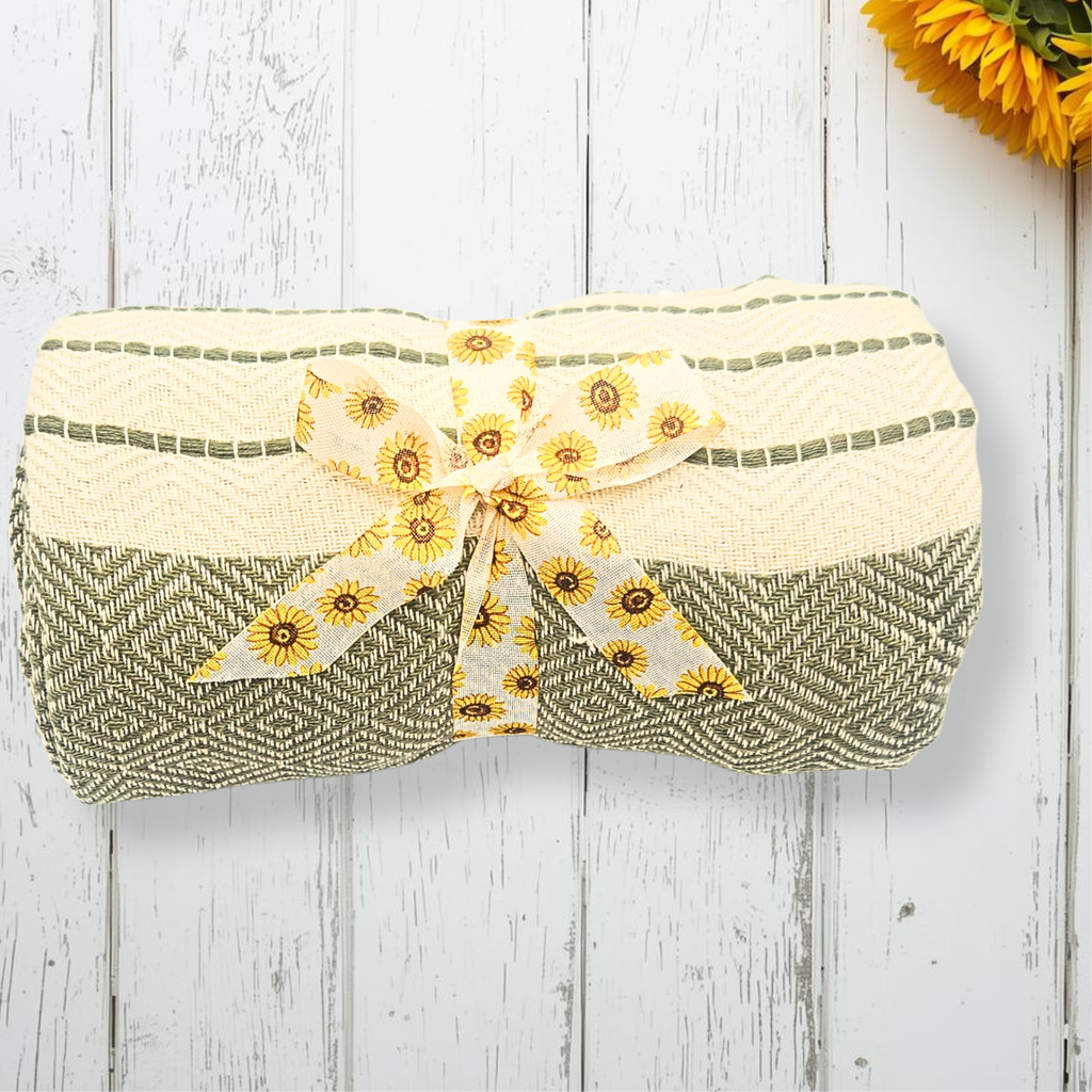 Green and beige throw with a sunflower ribbon on a wooden surface