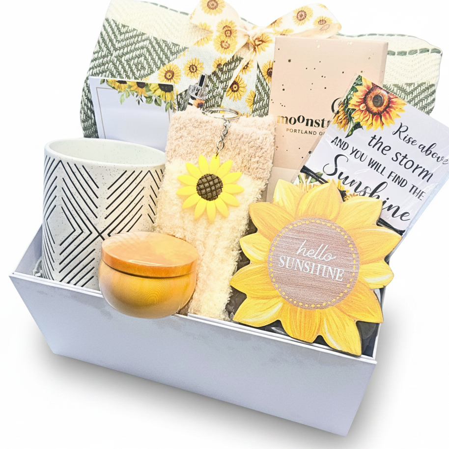 A curated gift box filled with sunflower-themed items, including a yellow sunflower-shaped decor reading 'hello sunshine,' a mug with black geometric lines, a small round candle, a decorative throw, and a greeting card.