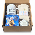 A curated gift set containing a white ceramic mug, cozy cream-colored knit sockss with a 'THANK YOU' band, a blue bag of Pillsbury soft chocolate chip cookies, and a small round tin lotion bar, all arranged in a kraft box with shredded paper filler.