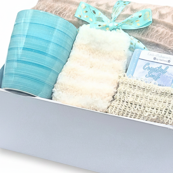 Gift box with blanket wrapped in a teal ribbon, mug, socks, soap, and soap saver bag on a neutral background.