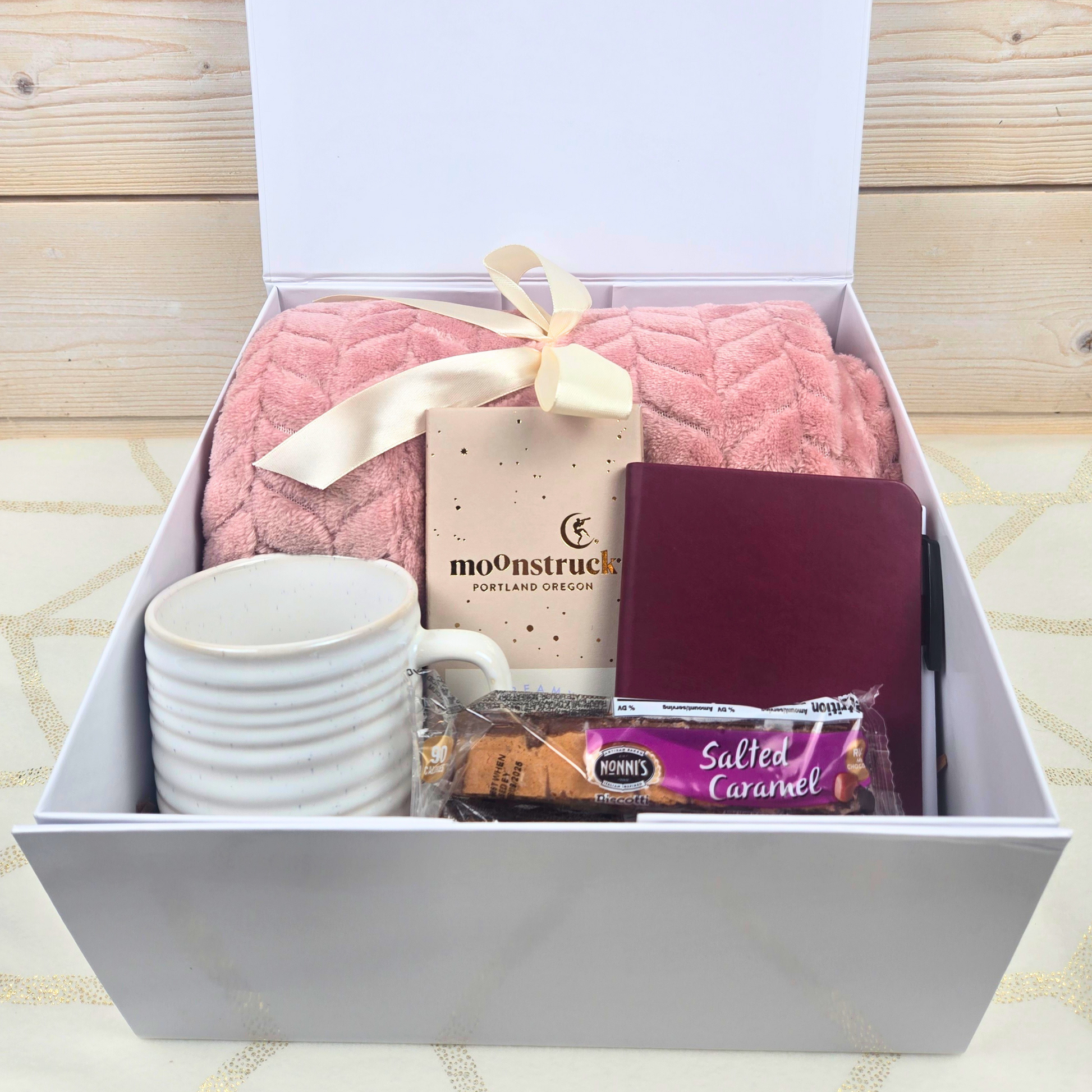 Gift Box for Her featuring a cozy blanket, a stylish mug, a chic notebook, a rich chocolate bar, and indulgent Ferrero Rocher chocolates. Perfectly curated for a relaxing and thoughtful gift experience.