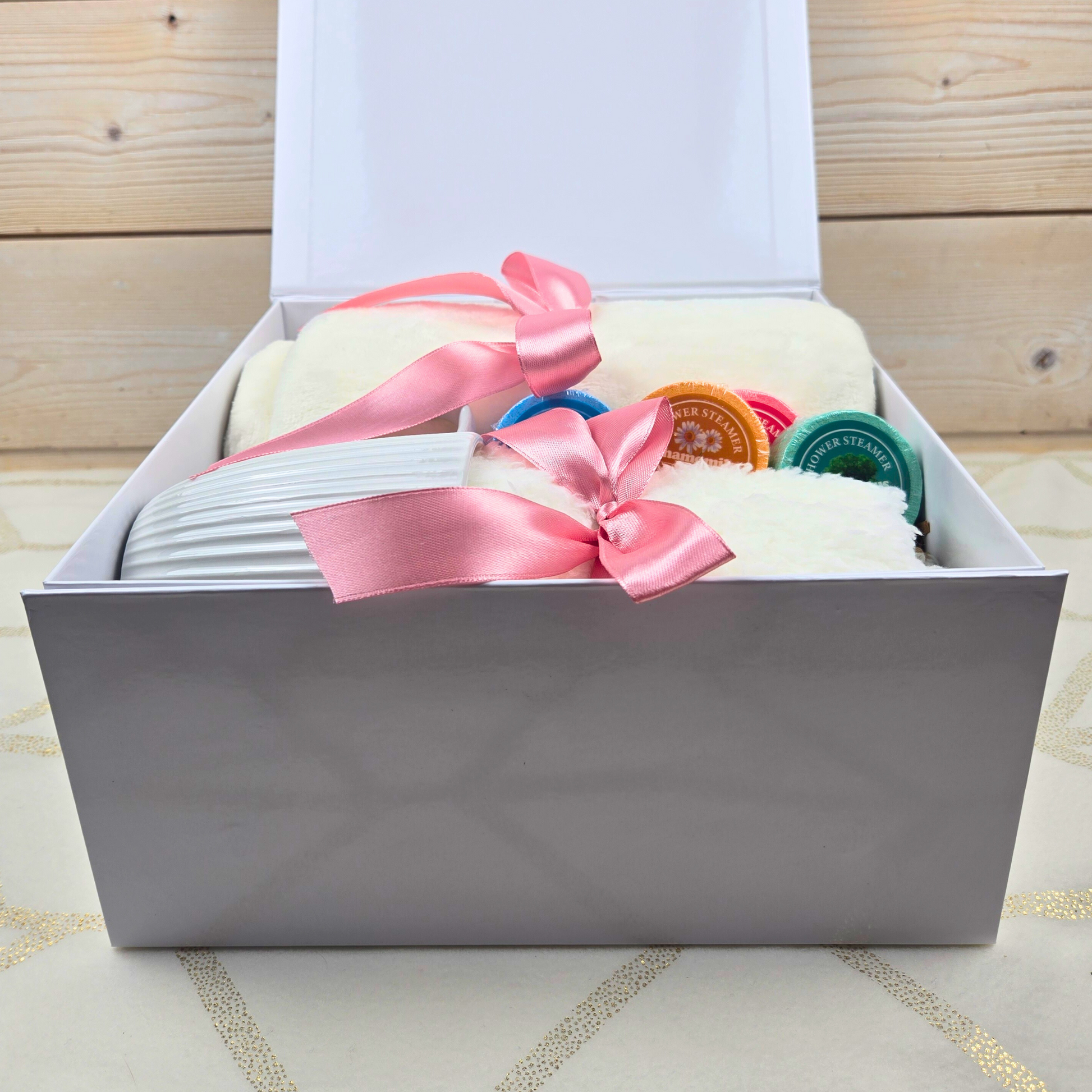 Cozy gift box featuring a soft blanket, a charming mug, fuzzy socks, and invigorating shower steamers for a perfect self-care experience.