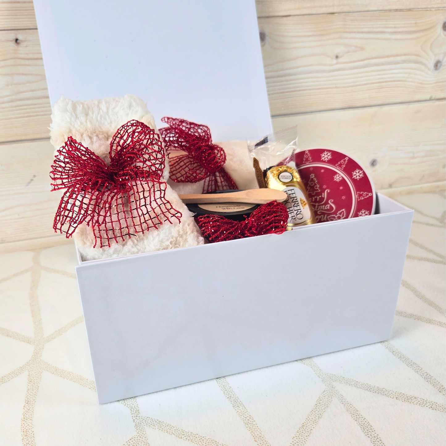 Festive holiday gift box with a magnetic lid, packed with a plush blanket, stylish coaster, soothing sugar scrub, and delicious Ferrero Rocher chocolates, side view.